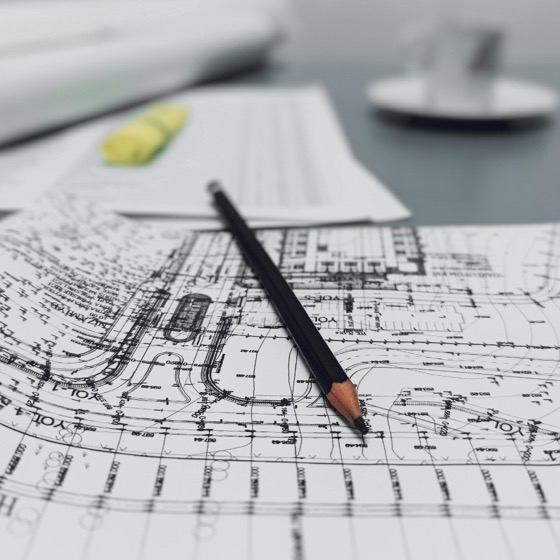 Technical site drawings and blueprints on a desk with pencil during planning review.
